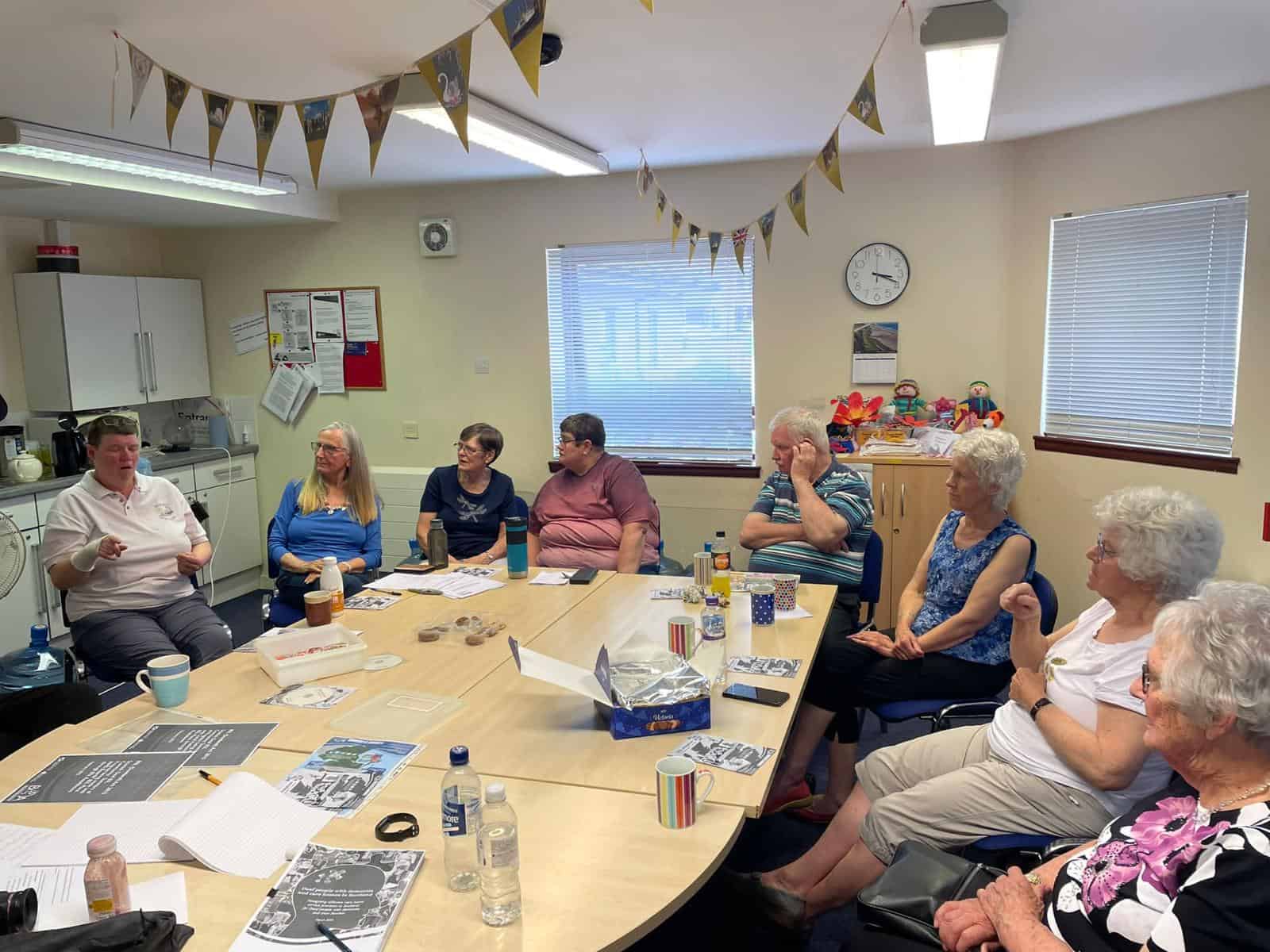 Community meeting discussing the BSL (Scotland) Act 2015 in a room with elderly participants.