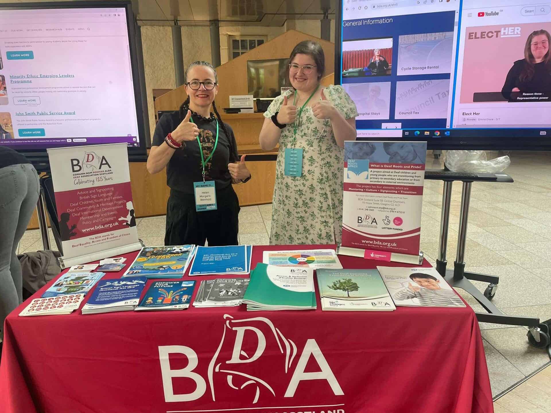 Two women at BSL Act 2015 awareness booth giving thumbs up.