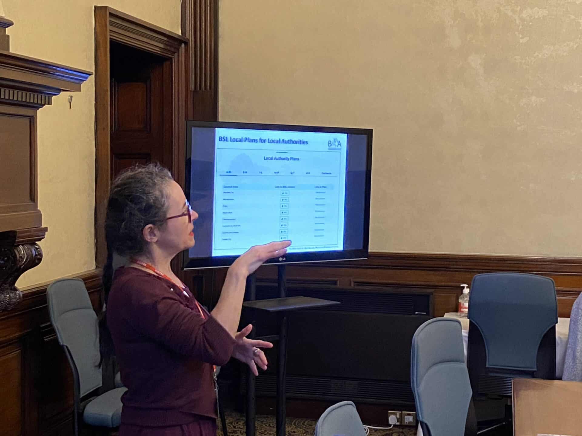 Woman presenting information on BSL (Scotland) Act 2015 at a meeting.
