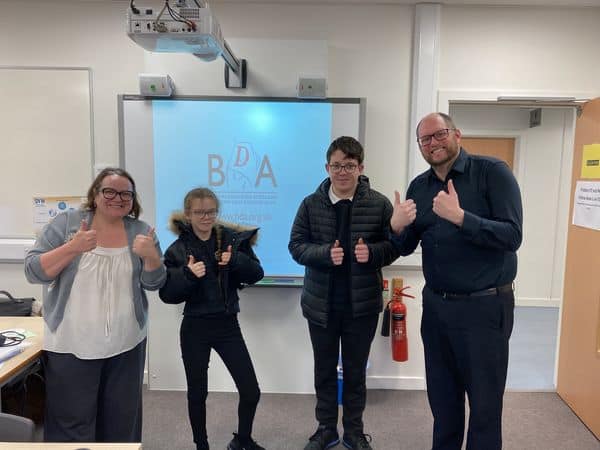 Group of people in a classroom giving thumbs up, BSL Act 2015 awareness.