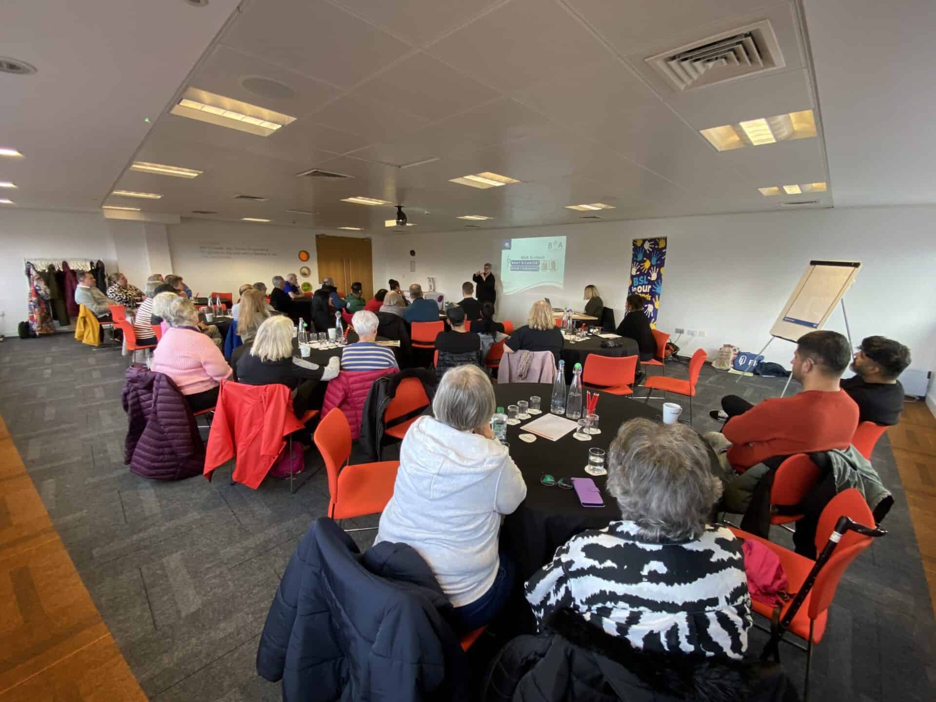 People attending a conference on the BSL (Scotland) Act 2015 in a meeting room.