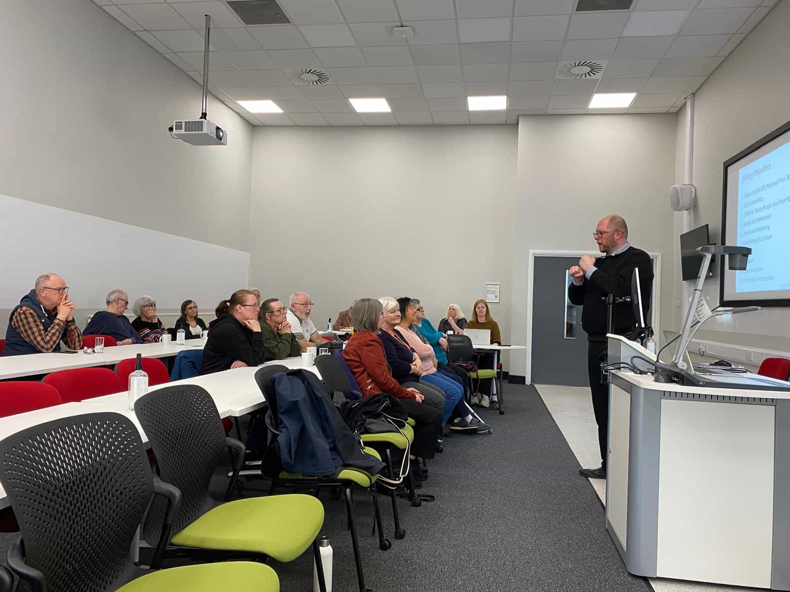 Sign language interpreter speaking to a group about the BSL Act 2015 in a classroom.