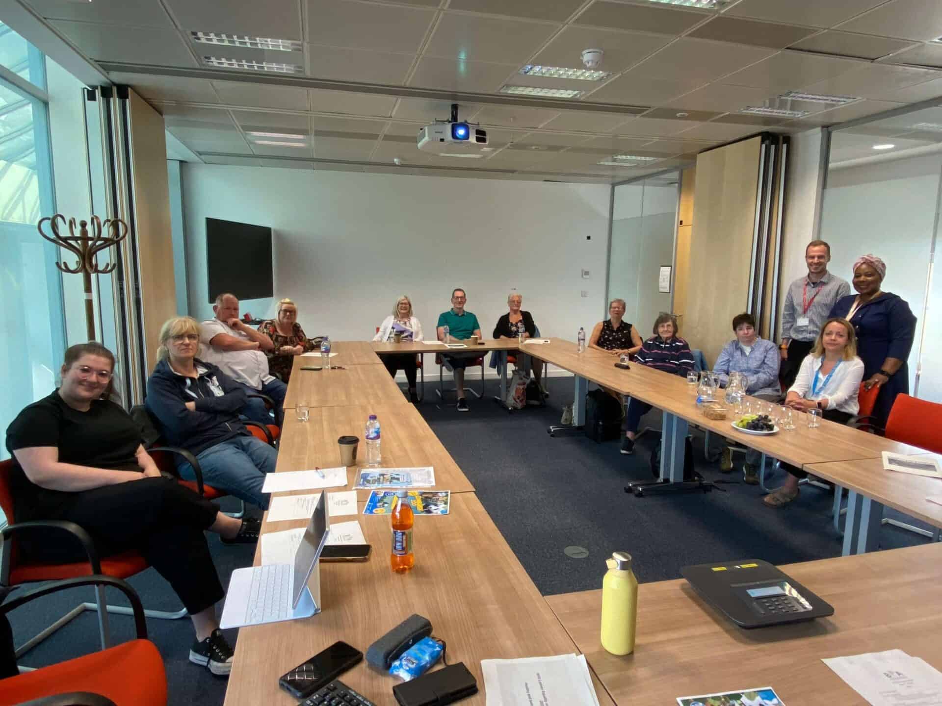 Group of people in a meeting room, some using sign language, discussing BSL legislation.