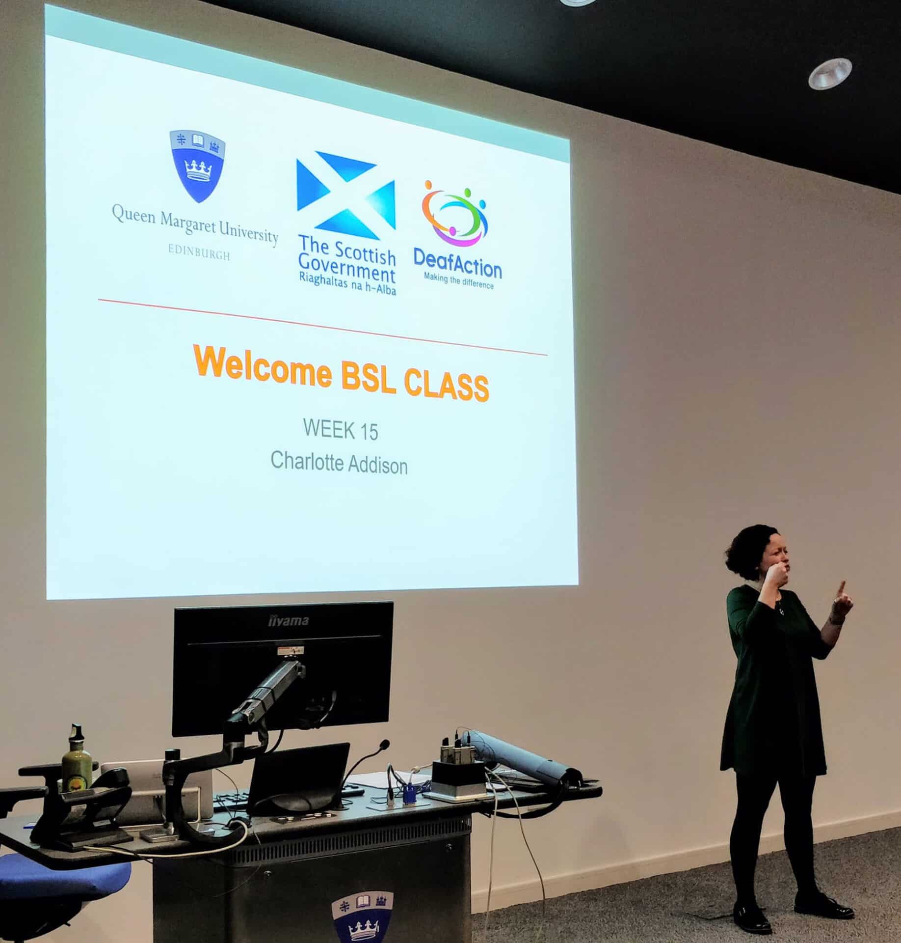 Speaker presenting at BSL Scotland Act 2015 event in front of screen.