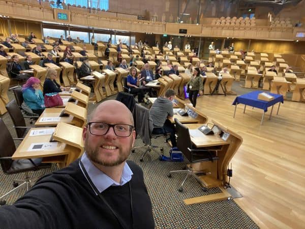 Man taking selfie at Scottish Parliament during BSL Act 2015 discussion.