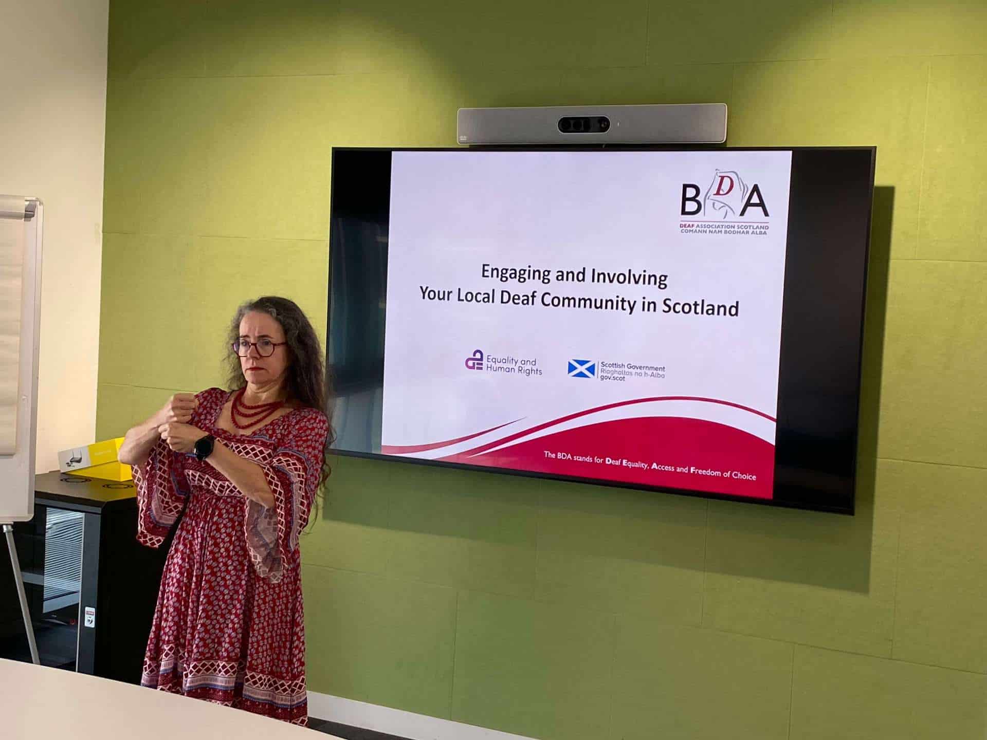 Woman presenting at BSL Act 2015 event in Scotland with screen.