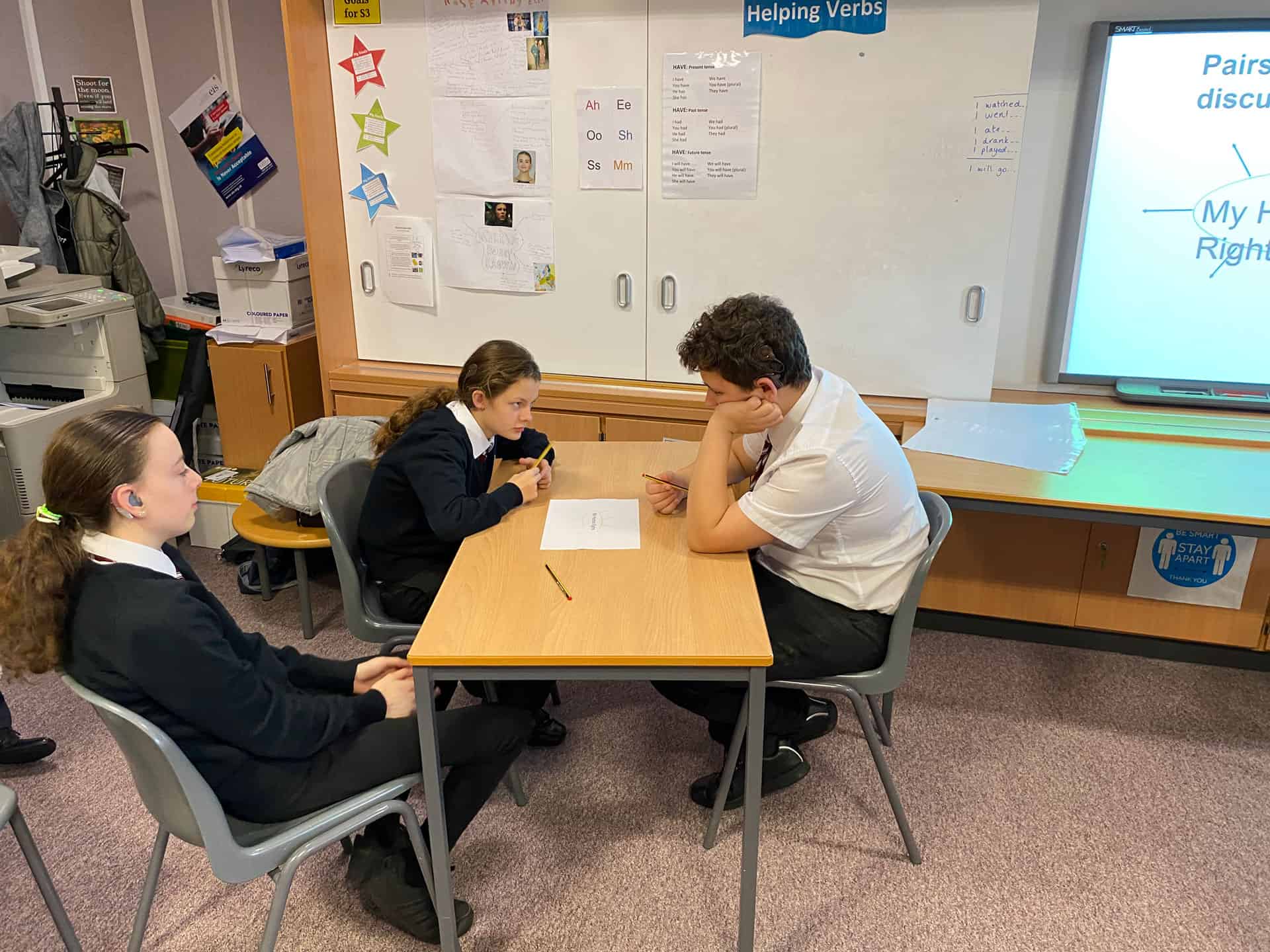 Teacher assisting students with learning in a classroom setting in Scotland.